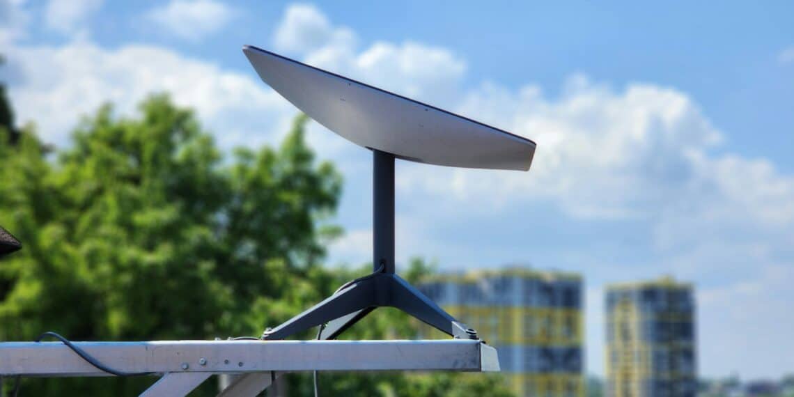 Antena Starlink ao ar livre com edifícios ao fundo, em dia ensolarado.