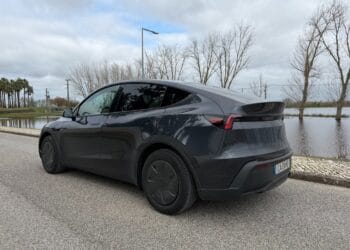 Tesla Model Y elétrico preto estacionado à beira de um lago, com árvores ao fundo, em um dia nublado.